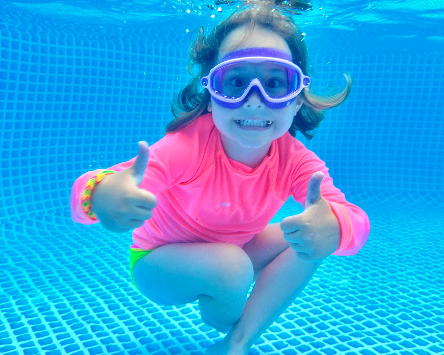 Girl under water smiling giving thumbs up wearing a neon pink coral rash guard and neon yellow swm bottoms from HiViz neon swimwear. Highly visible swimwear for kids.